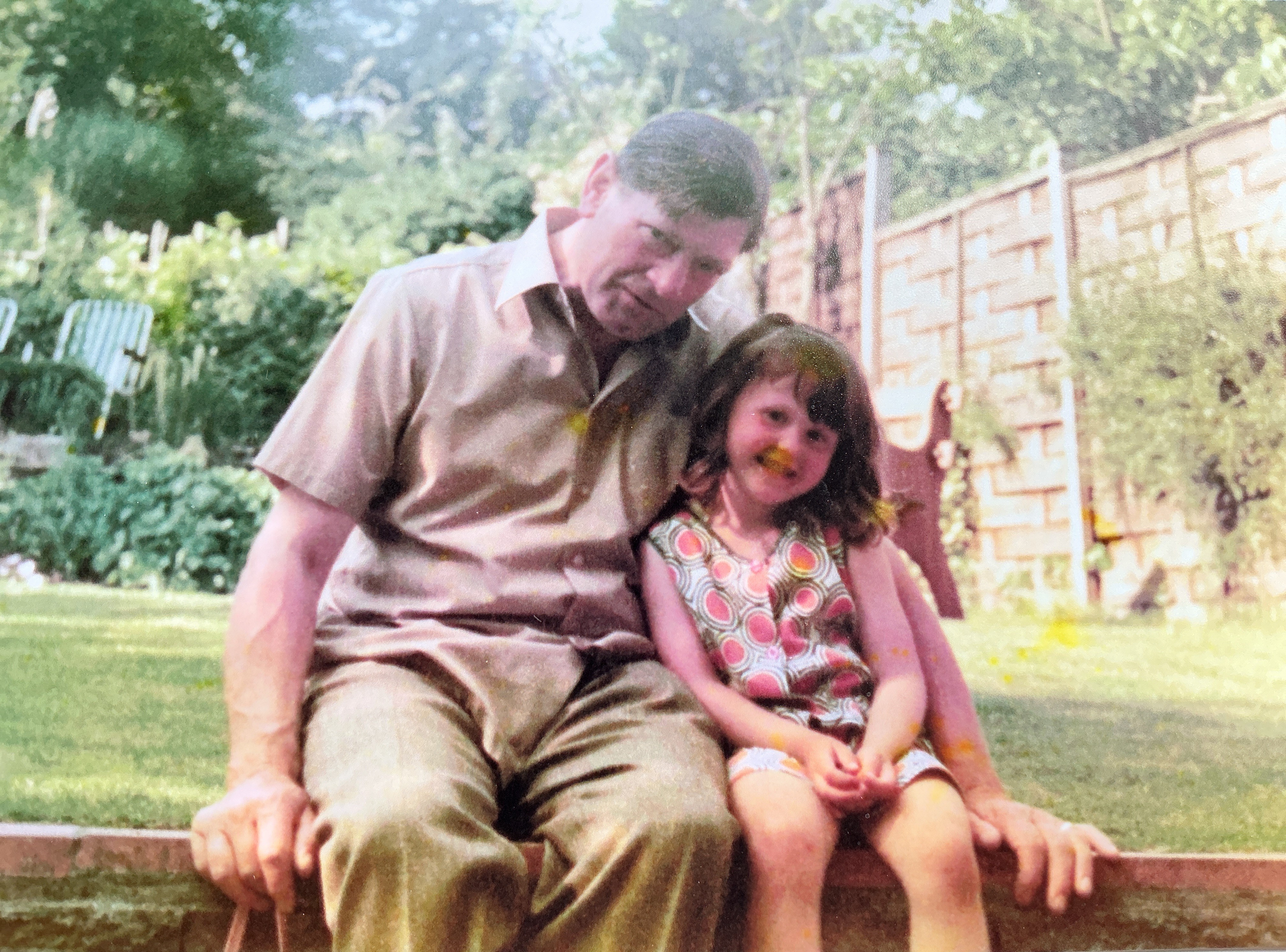 A grandfather and his granddaughter sitting together in a garden
